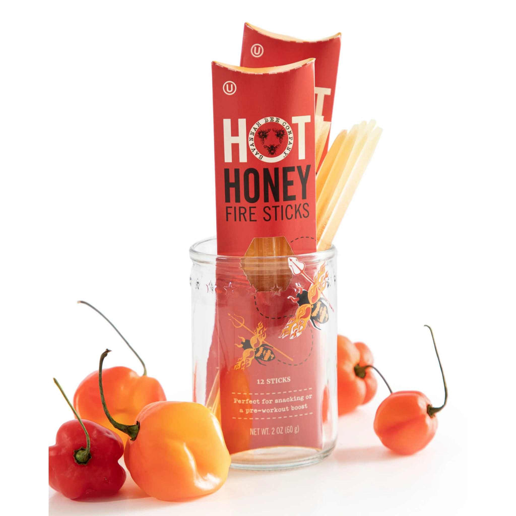Hot Honey Fire Sticks 12 pack from Savannah Bee Company. Two packs plus a bunch of single straws sitting in a jar surrounded by peppers.