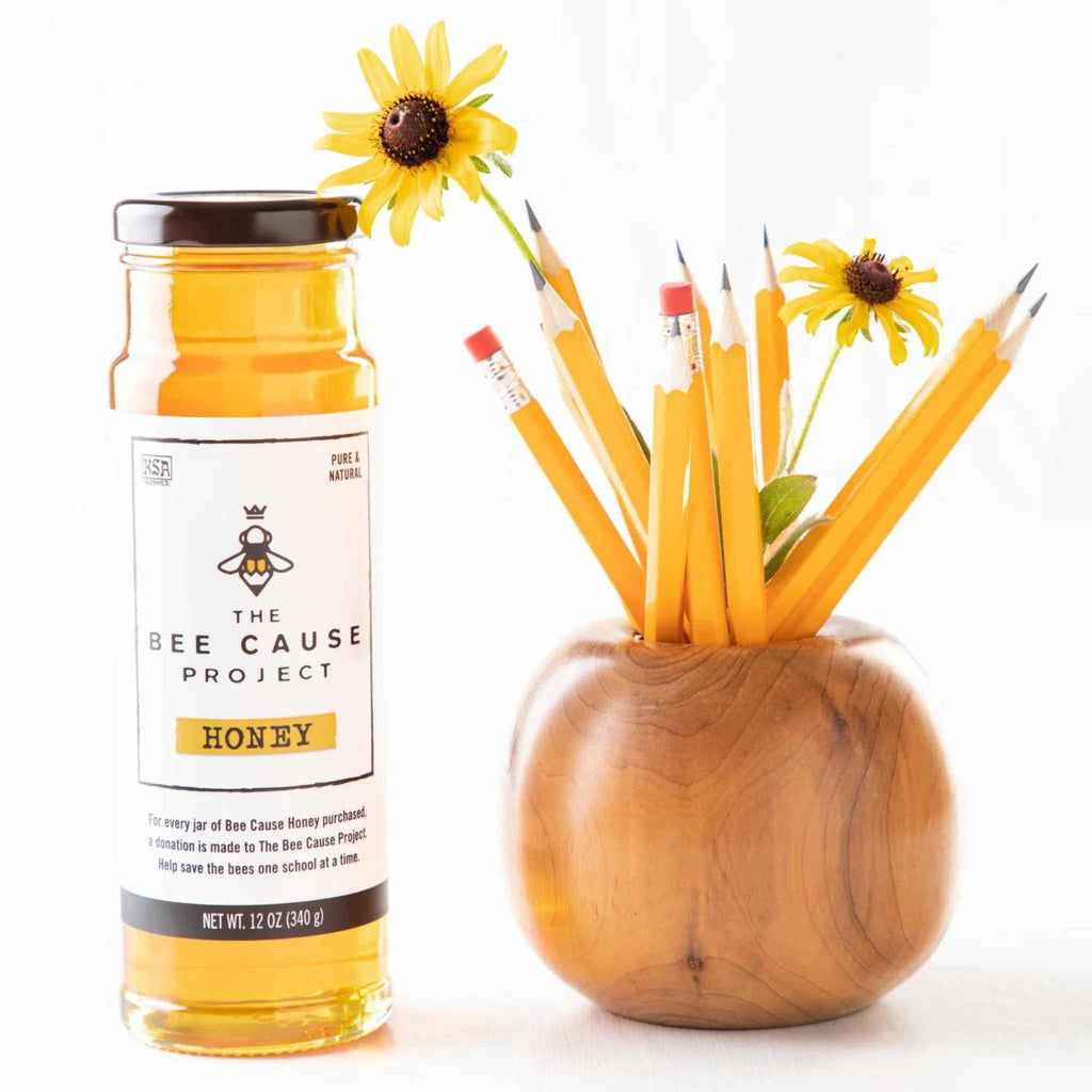 The Bee Cause Project Honey 12 oz. from Savannah Bee Company next to a wooden vessel filled with pencils and flowers.