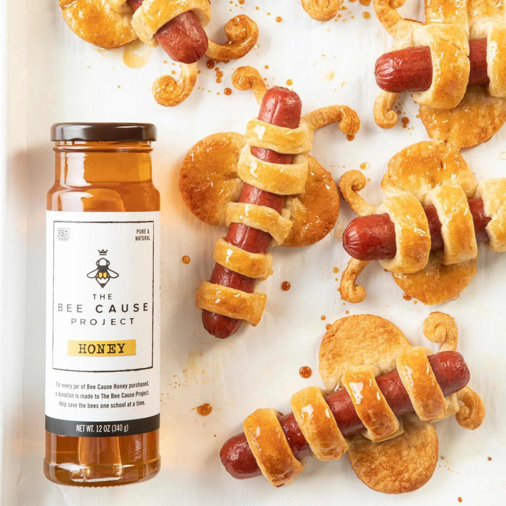 The Bee Cause Project Honey 12 oz. from Savannah Bee Company laying next to pigs in a blanket.